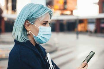 Gorgeous caucasian entrepreneur with blue hair posing with modern gadgets while wearing an anti flu mask - Powered by Adobe