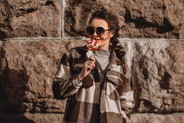 Young woman with candy on a stone wall background in fashionable clothes