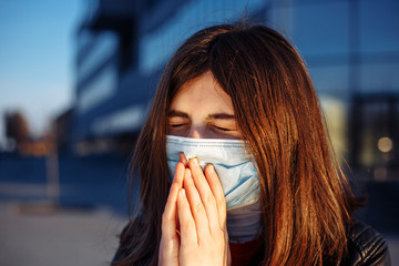 Young girl sneezes and coughs in a medical mask near a closed shoppong mall. She feels fewer and...