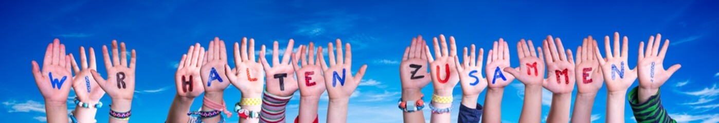 Children Hands Building Colorful German Word Wir Halten Zusammen Means Together We Are Stron. Blue Sky As Background