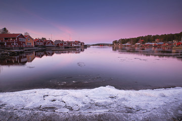 Panorama at sunset over a bay with ice in the foreground and small red cottages on each side of the bay