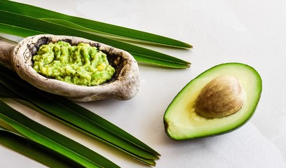 An avocado appetizer in a large wooden spoon and half fruit with a bone lie on a white background. Avocado Sauce. Gualamole.