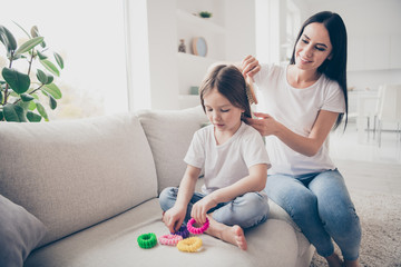 Happy sweet adorable two people loving mommy make haircut ponytail brush comb her little kid daughter sit crossed legs bare foot in apartment indoors