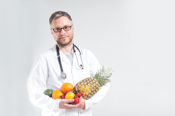 smiling doctor in a coat holding fruits in his hands on a white background