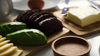 Perfect breakfst. Morning breakfast with cheese, avocado, butter, brown bread, egg. Girl's hand puts white cup or mug with smudges black aromatic coffee on the table.