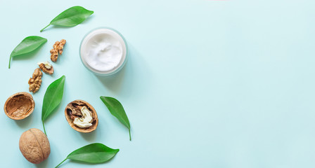 Cream bottle with  fresh green plant leaves and walnuts on blue  background. Concept natural cosmetics. Aromatherapy treatment. Top  view and copy space flat lay. 