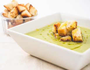 Green vegetables soup and croutons served in a white plate with olive oil. Side angle with white background. 