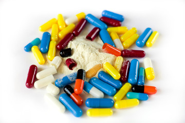 many multi-colored medical capsules and white powder, substance, on a white background, top view, closeup, isolate