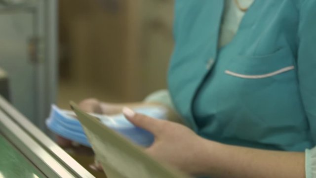 Medical mask on conveyor belt in the workshop of factory for production of medical clothing. Production of disposable medical clothing for protection against the virus. Manufacture of medical masks.