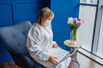 Portrait of european girl in white viral protective costume and face mask working from home on...