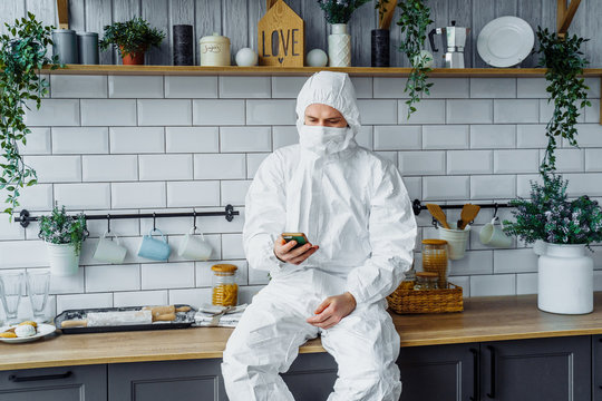Portrait of european man wearing protective white suit with hoodie and face mask works from home with phone and solvs important business. Quarantined and isolated due to coronavirus epidemic