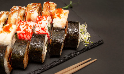 Sushi on a black slate blackboard with various ingredients, micro-greens and chopsticks on a black background with copy space