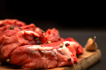 Raw sliced ​​beef meat sprinkled with pepper on a wooden cutting board with copy space