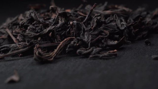 Black or green tea leaves fall on a black table. Black background on which the petals of tea are spinning.