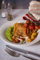 Roast pork chop with mushy peas, potatoes and tomatoes on white plate