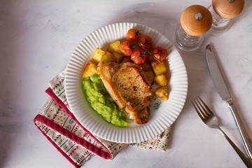 Roast pork chop with mushy peas, potatoes and tomatoes on white plate. View from above, top view