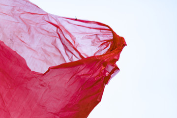 A red plastic bag in close-up develops in the wind against a bright sky. A grocery polymer packet flies in the air picked up a fresh spring breeze in a clear sky in the evening, screensaver