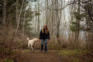 Young woman walking her yellow labrador retriever dog in the forest alone