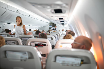 Pretty, young woman aboard an airplane during a lang haul commercial flight - stretching her legs a...