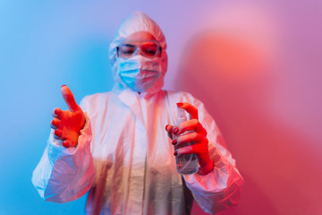 Female doctor in protective suit in lab coat, defensive eyewear and mask standing with antibacterial spray. Stop coronavirus. COVID-19.