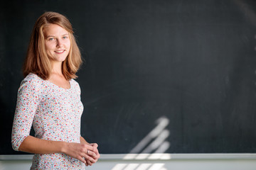 Pretty, young female student/young teacxher in front of a blackboard during class