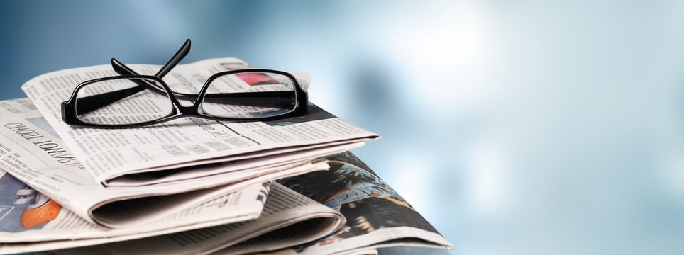 Pile of newspapers stacks and glasses on blur background
