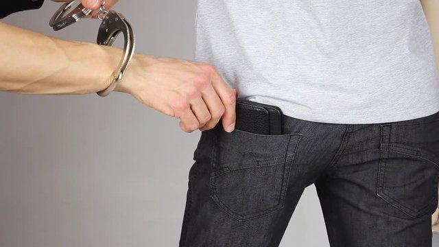 pickpocket hand gently try to takes out leather wallet from someones black pants back pocket, but hand of justice puts on handcuffs, pickpocketing theft crime and punishment, close-up 