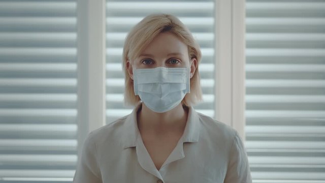 Woman is looking at the camera in isolation at home for a virus outbreak or hypochondria. Wearing face protection mask in the prevention of Coronavirus, ebola, TB and other diseases. Protect yourself.