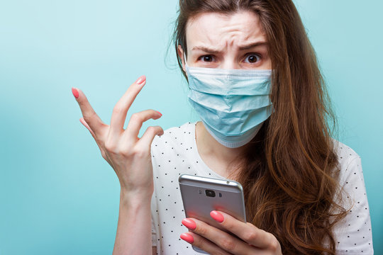 Isolation during a coronavirus epidemic. A girl in a disposable medical mask and hospital clothes holds a smartphone in her hand. Indignant, angry, nervous due to shocking news