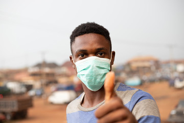 young handsome african man wore face mask preventing, prevent, prevented himself from the outbreak in his society and did thumbs up.