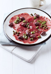Carpaccio with Kalamata Olives, Capers and Olive Pesto. Bright wooden background. 
