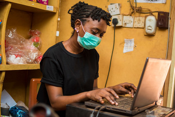 young beautiful nigerian attendant wearing face mask in the supermarket as she's operating the...