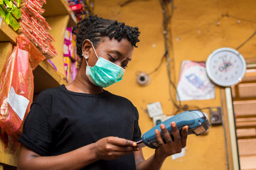 young african female attendant using the point of sale machine to pay for the goods her customer...