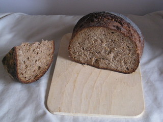 pedazo de hogaza de pan de de centeno sobre tabla de madera con cuña cortada al lado sobre mantel blanco