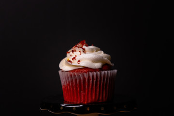 red velvet cupcake with white cream cheese icing and colorful sprinkles on a black background