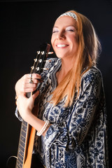Youth Life Concepts. Portrait of Smiling Caucasian Blond Girl Posing With Guitar In Studio Against Black.