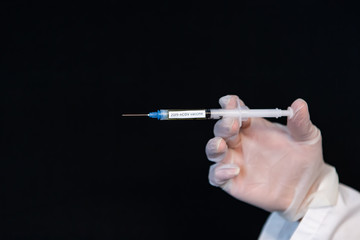 Selective focus closeup, syringe holding red liquid labeled 2019-nCOV vaccine being held by a gloved hand horizontally over a black background 