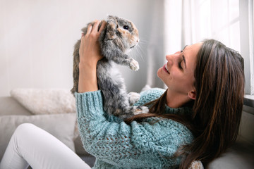Adorable furry pet bunny rabbit and beautiful woman alone indoors at home, bonding, hugging,...