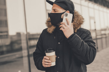 Men using phone, wears a black protective medical face mask being in the city during a coronavirus...