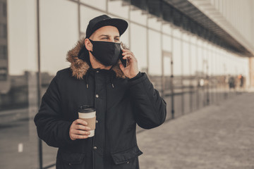 Men using phone, wears a black protective medical face mask being in the city during a coronavirus pandemic. Protection from viruses in the city.
