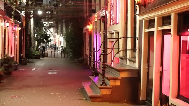 Panning shot of a nearly empty street in the Amsterdam Red Light District. Prostitute's windows in the foreground. Nighttime.