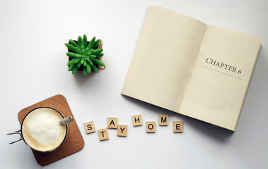 Fototapeta na wymiar Stay Home in Quarantine: photo of a cup of coffee, a book and wood tile letters spelling 
