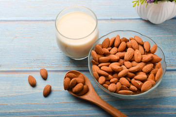 Close up view of healthy almond milk in drinking glass with seed in bowl on wooden background.