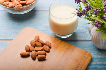 Close up view of healthy almond milk in drinking glass with seed in bowl on wooden background.