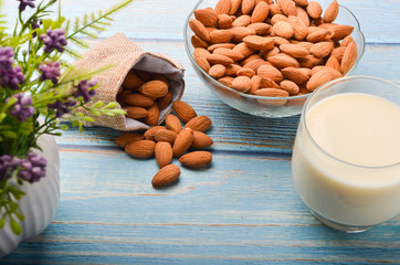 Close up view of healthy almond milk in drinking glass with seed in bowl on wooden background.