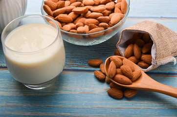 Close up view of healthy almond milk in drinking glass with seed in bowl on wooden background.