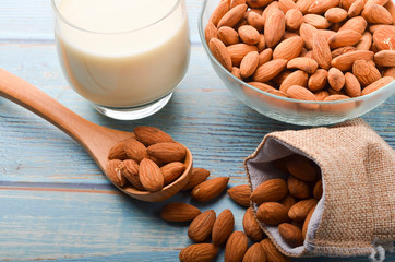 Close up view of healthy almond milk in drinking glass with seed in bowl on wooden background.