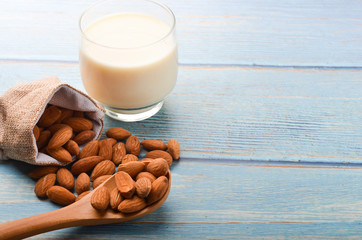 Close up view of healthy almond milk in drinking glass with seed in bowl on wooden background.