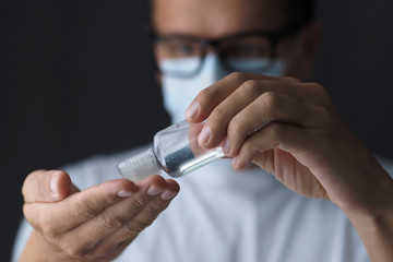 Man in medical mask using small transparent bottle sanitizer, alcohol gel. Selective focus.