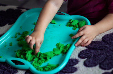 Hands of a child playing with green kinetic sand on a tray, selective focus. Children's creativity, antistress, close-up